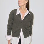 A person wears a dark green brushed wool button-front Roselle Knit Cardigan by Herskind ApS over a light pink collared shirt and black trousers.