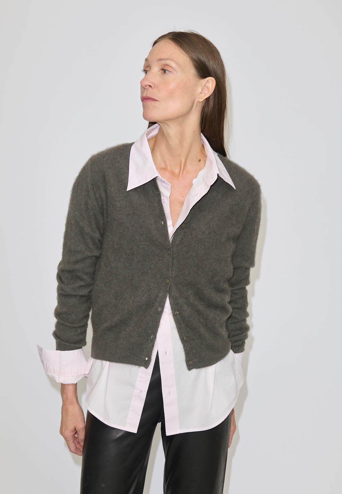 A person wears a dark green brushed wool button-front Roselle Knit Cardigan by Herskind ApS over a light pink collared shirt and black trousers.