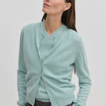 A woman wears a light blue, brushed wool Roselle Knit Cardigan by Herskind ApS over a matching V-neck sweater.