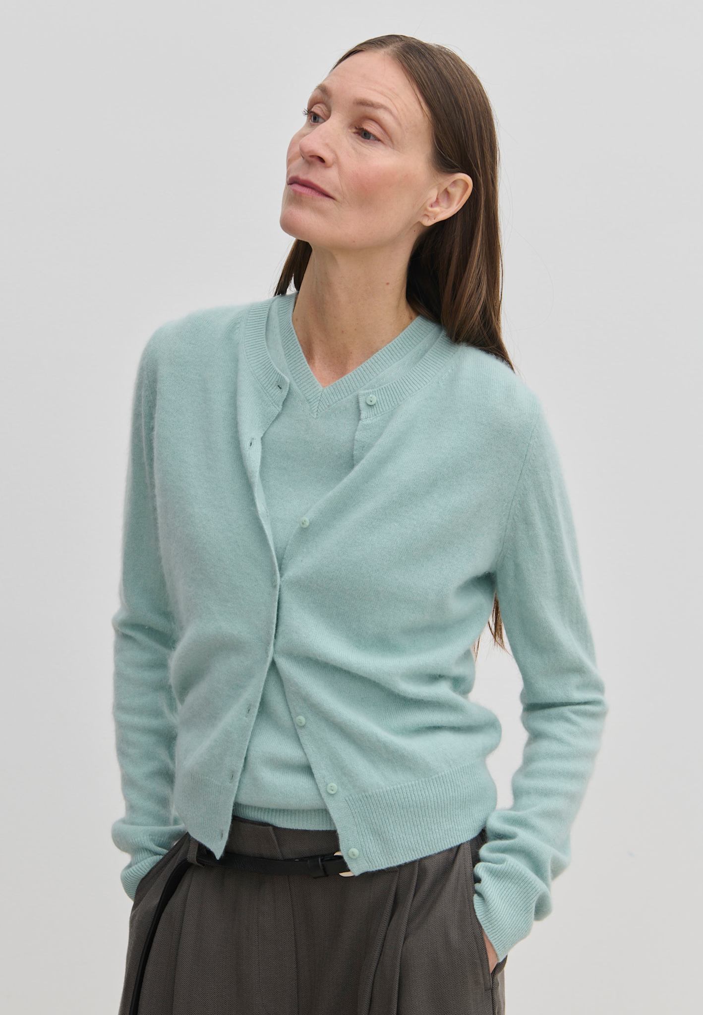 A woman wears a light blue, brushed wool Roselle Knit Cardigan by Herskind ApS over a matching V-neck sweater.