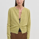 A lime green brushed wool Roselle Knit Cardigan by Herskind ApS worn over a black lace camisole and a brown skirt.