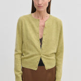 A lime green brushed wool Roselle Knit Cardigan by Herskind ApS worn over a black lace camisole and a brown skirt.