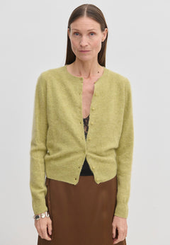 A lime green brushed wool Roselle Knit Cardigan by Herskind ApS worn over a black lace camisole and a brown skirt.