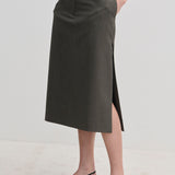 A person wearing a dark grey, straight-silhouette Herskind ApS Collin Mid waist Skirt with a side slit and black kitten-heel slingback shoes.