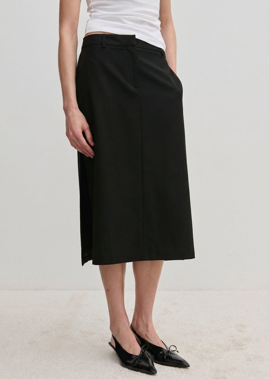 A person wearing a white top and the black Collin Mid waist Skirt, a midi-length style with a front seam and straight silhouette.