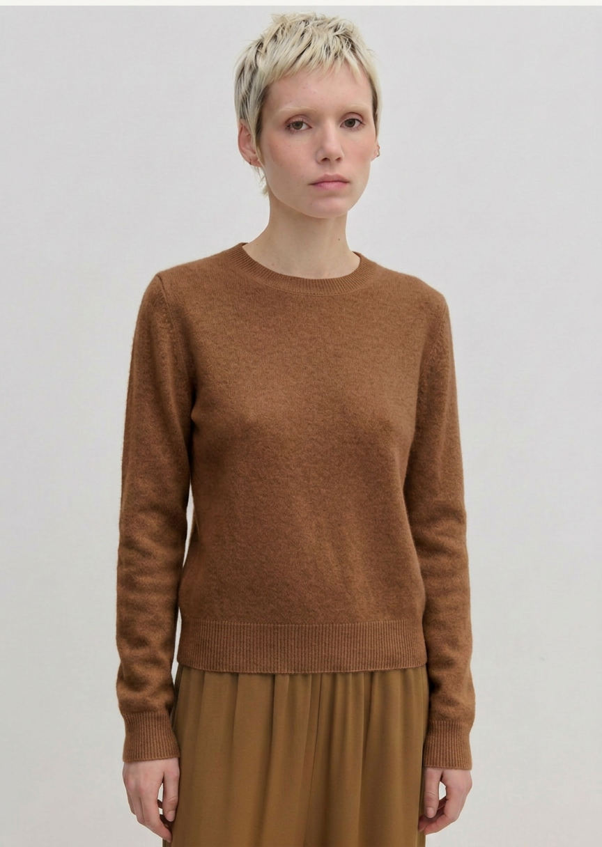 A person wearing an Elena Knit Blouse by Herskind ApS, featuring a long-sleeved, brown crew-neck knit design with a ribbed hem.
