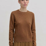 A person wearing an Elena Knit Blouse by Herskind ApS, featuring a long-sleeved, brown crew-neck knit design with a ribbed hem.