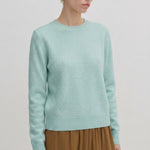 A person wearing a pale green Herskind ApS Elena Knit Blouse with a crew neck and a ribbed hem.