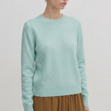 A person wearing a pale green Herskind ApS Elena Knit Blouse with a crew neck and a ribbed hem.