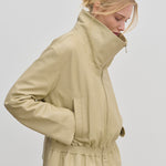 A person wearing the cream-colored Herskind ApS Sully Leather Jacket, featuring an oversized funnel neck and a smocked, elasticized waist.