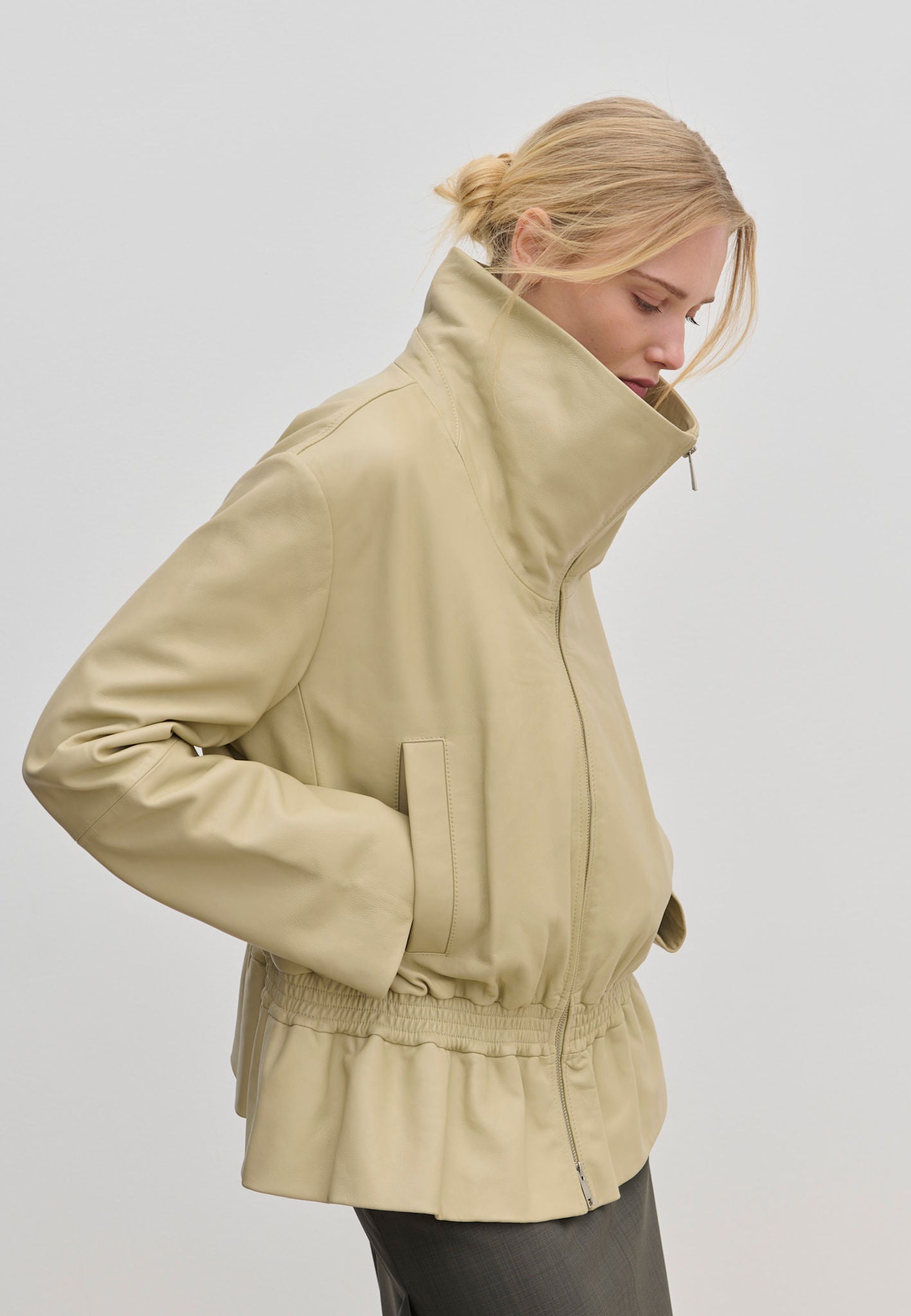 A person wearing the cream-colored Herskind ApS Sully Leather Jacket, featuring an oversized funnel neck and a smocked, elasticized waist.