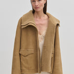 An oversized tan suede Nicole Shearling Jacket by Herskind ApS with a wide collar worn over a pale slip dress.