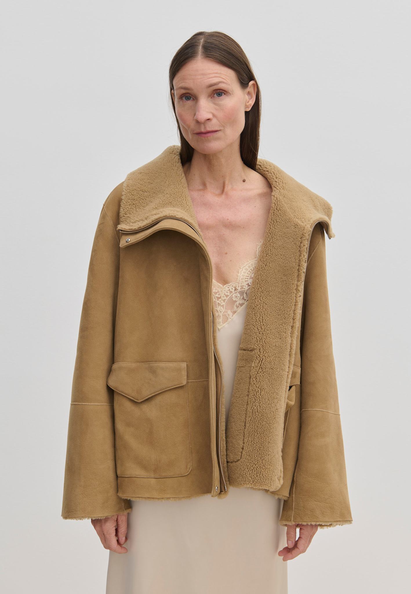 An oversized tan suede Nicole Shearling Jacket by Herskind ApS with a wide collar worn over a pale slip dress.