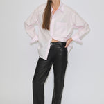 A person wearing a pale pink button-down shirt and high-waisted, straight-fit black Cooper Leather Jeans by Herskind ApS, with their hands on their hips.