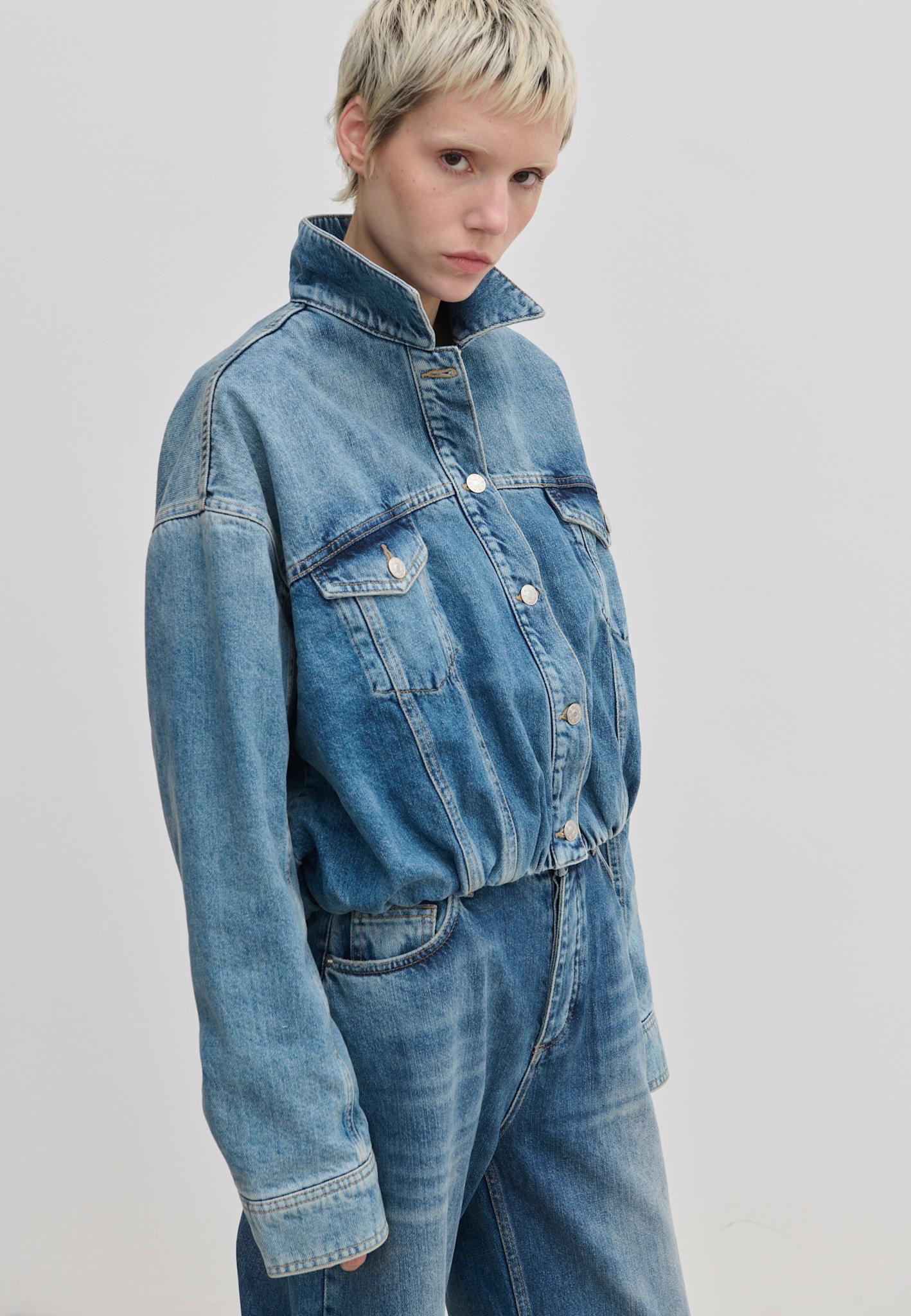 A person wearing a cropped organic cotton Illy Denim Jacket by Herskind ApS with a high collar, button-front closure, and chest pockets.