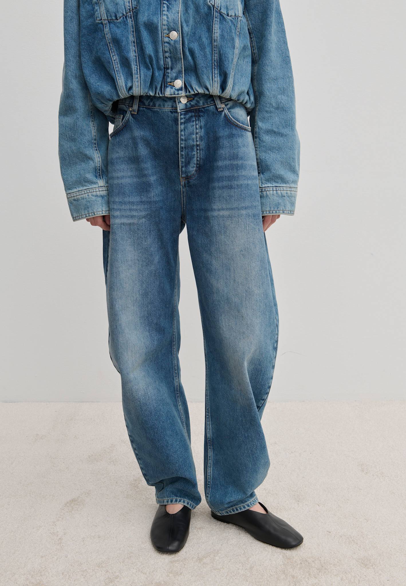 A person wearing a denim jacket, Freya Denim Jeans (32 - Long) with a relaxed-fit, barrel-leg shape, and black flat shoes.