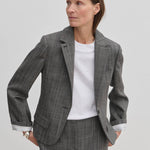 A person wearing a grey plaid Dakota Fitted Blazer by Herskind ApS over a white t-shirt, with the sleeves rolled up to reveal white striped lining.