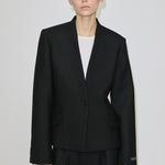 A person wears a black, single-button, fitted Higgins Fitted Blazer by Herskind ApS with a notched neckline over a white top.