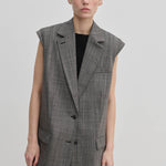 A person wearing a structured, sleeveless grey plaid Herskind ApS Cohen Sleeveless Blazer over a black top.