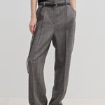 Herskind ApS Cambs Mid waist Pants in grey with a patterned design, wide leg silhouette, black belt, and pressed front creases, worn with a black top and black shoes.