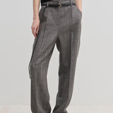 Herskind ApS Cambs Mid waist Pants in grey with a patterned design, wide leg silhouette, black belt, and pressed front creases, worn with a black top and black shoes.