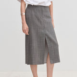 A person wearing a grey plaid Duncan Mid waist Skirt by Herskind ApS with a front slit, a white t-shirt, and pale shoes.