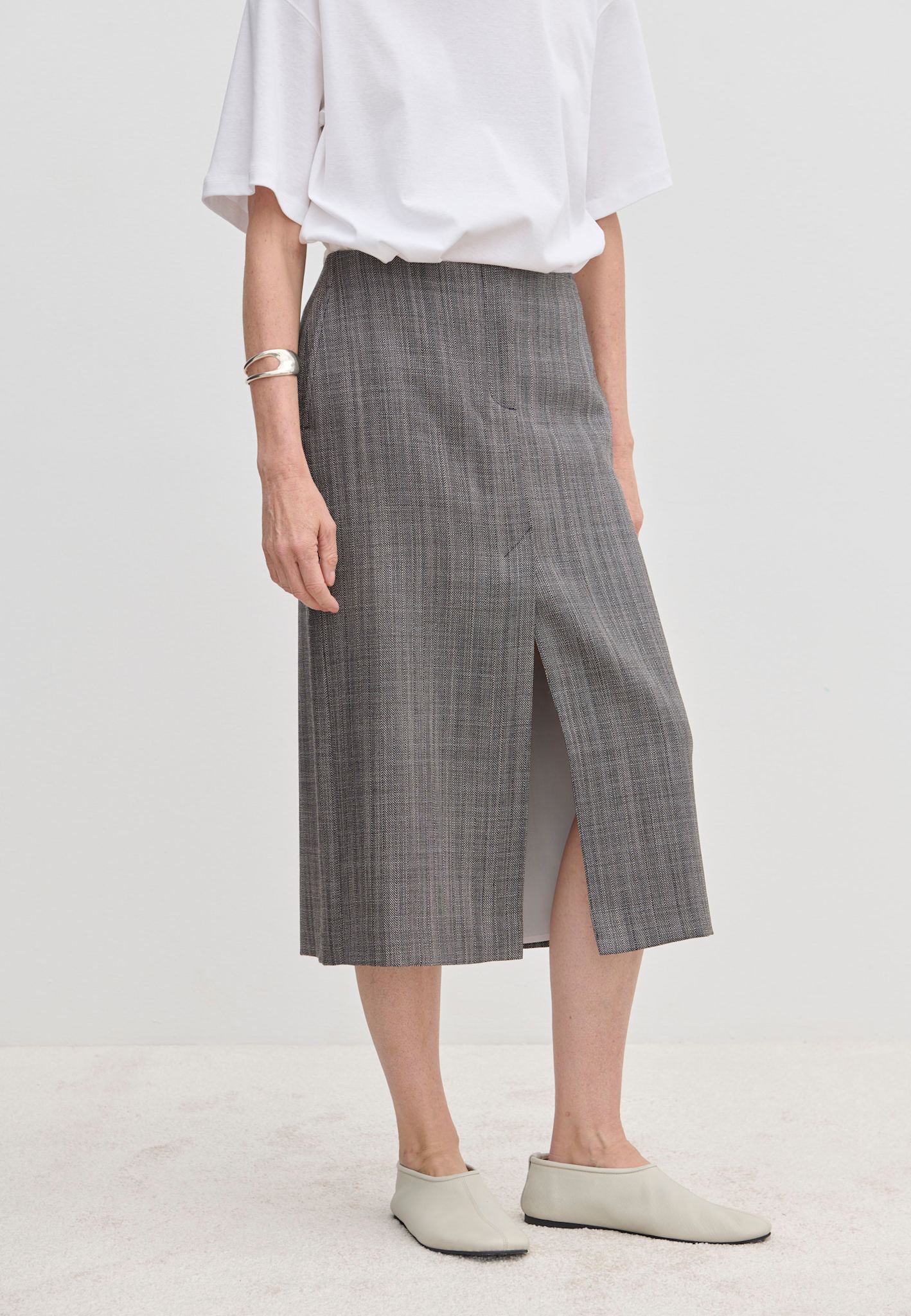 A person wearing a grey plaid Duncan Mid waist Skirt by Herskind ApS with a front slit, a white t-shirt, and pale shoes.