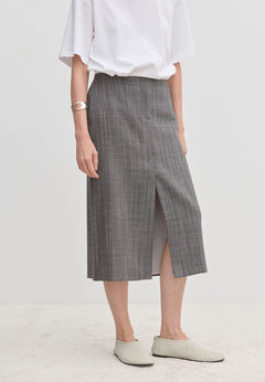 A person wearing a grey plaid Duncan Mid waist Skirt by Herskind ApS with a front slit, a white t-shirt, and pale shoes.