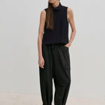A person wears a sleeveless black top and Herskind ApS Maddie Mid waist Baggy Pants, which feature a relaxed-fit, baggy silhouette with side pockets and buckled ankle cuffs.