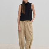 A woman wears a sleeveless black mock-neck top and beige Herskind ApS Maddie Mid waist Baggy Pants with buckled hems.