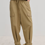Beige Maddie Mid waist Baggy Pants with a relaxed fit, featuring a drawstring waist, side cargo pockets, and buckled straps at the ankles.