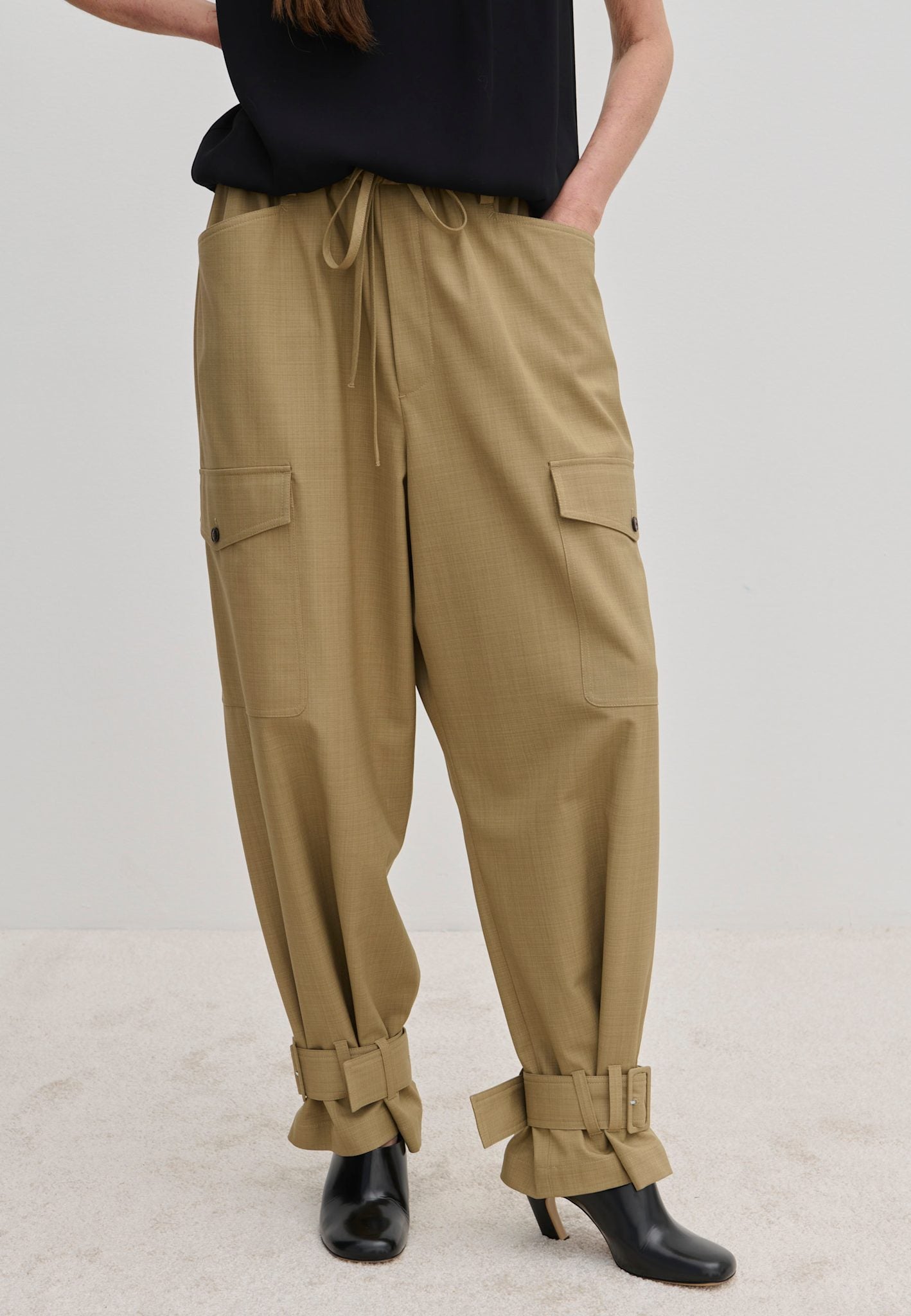 Beige Maddie Mid waist Baggy Pants with a relaxed fit, featuring a drawstring waist, side cargo pockets, and buckled straps at the ankles.