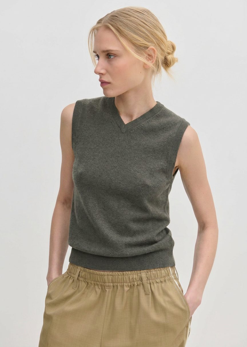 A person wearing an olive green Herskind ApS Fabien Knit Vest with a V-neckline.