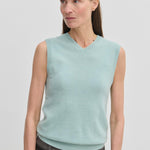 A woman wears a light blue V-neck Fabien Knit Vest by Herskind ApS over dark trousers.