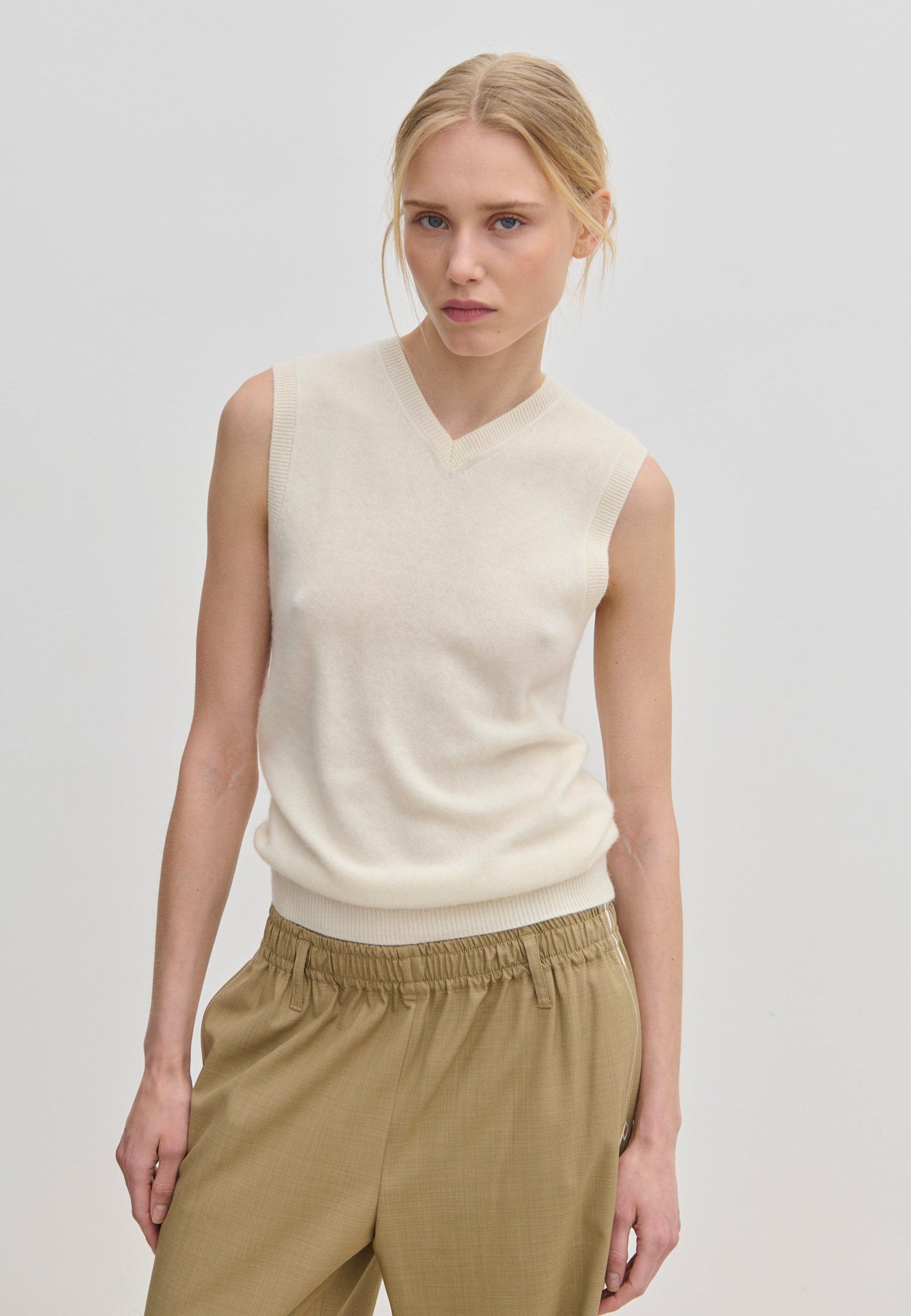 A model wearing a cream-colored Fabien Knit Vest and tan trousers.
