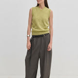 A person wearing a pale green Fabien Knit Vest tucked into charcoal wide-leg trousers with a black belt.