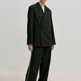 A person wearing a structured, double-breasted Herskind ApS Amalfi Regular Blazer and loose trousers with side stripes.