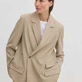 A person wearing an Amalfi Regular Blazer by Herskind ApS, a beige double-breasted style with structured shoulders and flap pockets over a white crew-neck shirt.