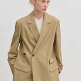 A person wearing a tan Amalfi Regular Blazer by Herskind ApS with structured shoulders over a white V-neck sweater.