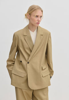A person wearing a tan Amalfi Regular Blazer by Herskind ApS with structured shoulders over a white V-neck sweater.