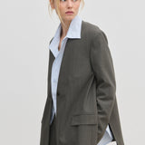 A person wearing a Clarissa Regular Blazer with modern, structured shoulders in grey over a light blue collared shirt.