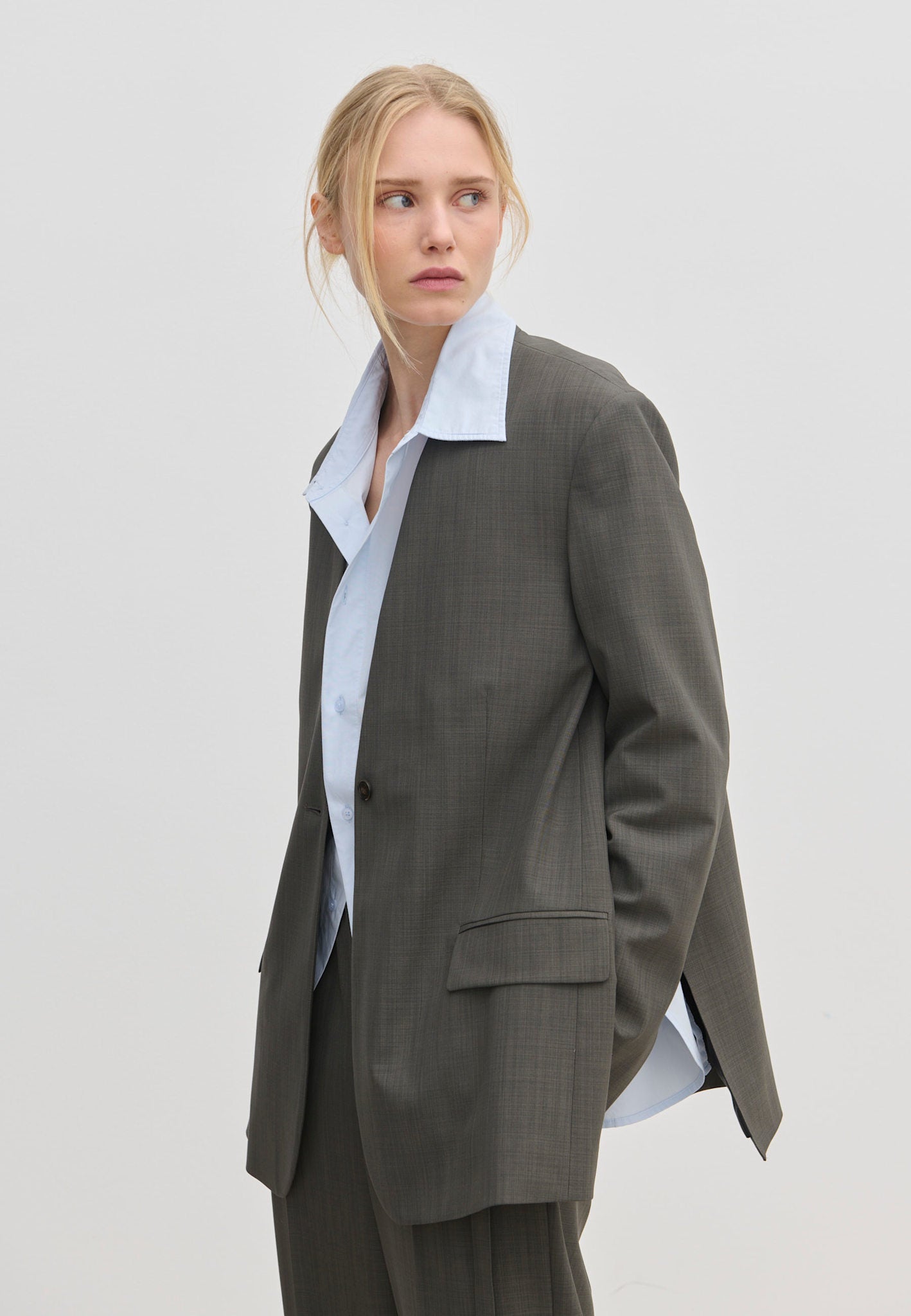 A person wearing a Clarissa Regular Blazer with modern, structured shoulders in grey over a light blue collared shirt.