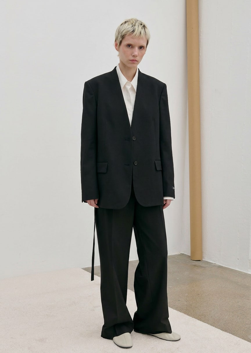 A person wears a modern, tailored black Clarissa Regular Blazer by Herskind ApS over a white collared shirt with matching black trousers.