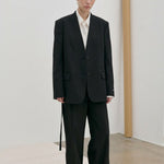 A person wears a modern, tailored black Clarissa Regular Blazer by Herskind ApS over a white collared shirt with matching black trousers.
