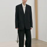 A person wears a modern, tailored black Clarissa Regular Blazer by Herskind ApS over a white collared shirt with matching black trousers.