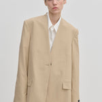 A model wearing an oversized, modern beige Herskind ApS Clarissa Regular Blazer with structured shoulders over a white collared shirt.
