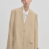 A model wearing an oversized, modern beige Herskind ApS Clarissa Regular Blazer with structured shoulders over a white collared shirt.