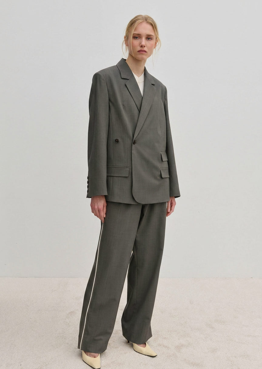 A woman wears a grey double-breasted blazer and matching Davi Mid waist Pants, which are mid-waist, wide-leg trousers with a vertical stripe down the side.