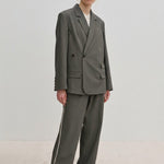 A woman wears a grey double-breasted blazer and matching Davi Mid waist Pants, which are mid-waist, wide-leg trousers with a vertical stripe down the side.