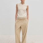 A person wearing a sleeveless V-neck sweater and Davi Mid waist Pants, which are mid-waist, wide-leg trousers with an elasticated waistband.